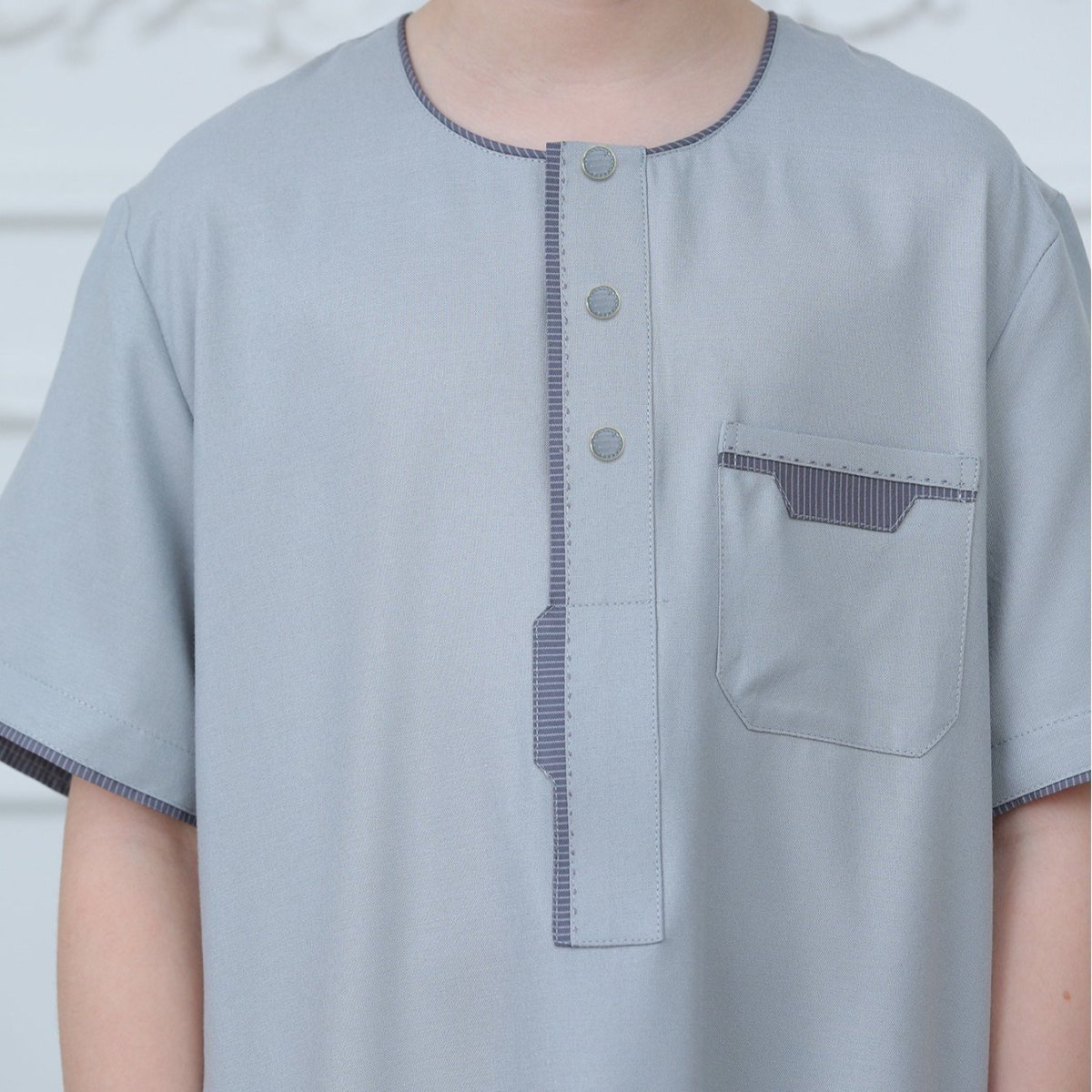 Close-up of silver snap button placket and charcoal contrast stitching detail on boys' thobe