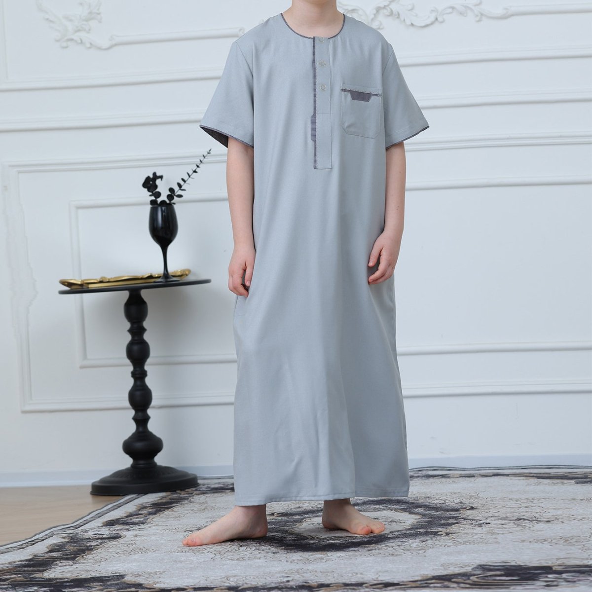 Front view of boys' powder blue thobe showing charcoal contrast piping on neckline and placket